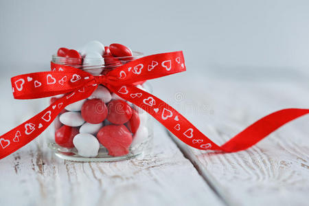 五颜六色的糖果罐装饰着红色的蝴蝶结，白色的木制背景上有心形。