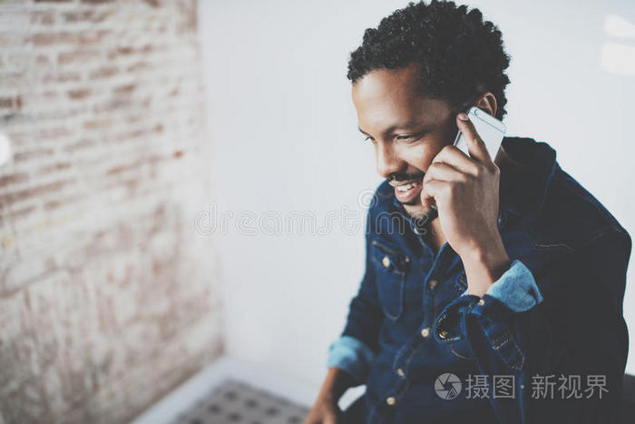 在现代家庭办公室，年轻的留着胡子的非洲男人在智能手机上进行对话的特写。概念人使用移动