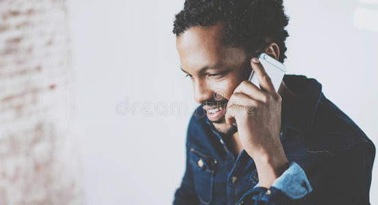 在现代家庭办公室，年轻的留着胡子的非洲男人在智能手机上进行对话的特写。概念人使用移动