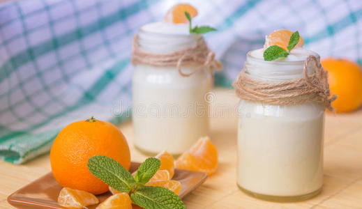 新鲜有机天然白色酸奶在玻璃瓶与橘子照片