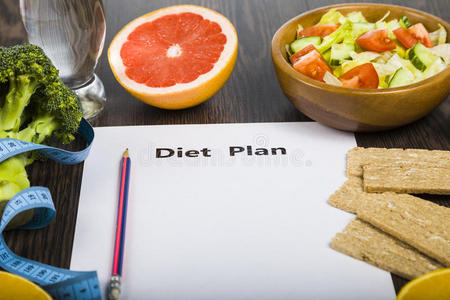 食物和一张纸，在一张深色的木制桌子上有一个饮食计划。