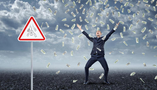 欣喜若狂的商人站在许多美元钞票下,从天上掉下来,附近有一个交通警告