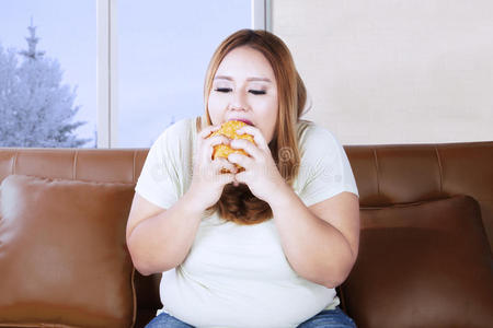 胖女人在沙发上吃汉堡包胖女人坐在厨房里吃垃圾食品.