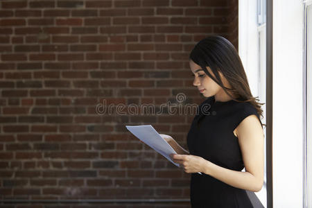 女商人站在办公室窗户旁阅读文件