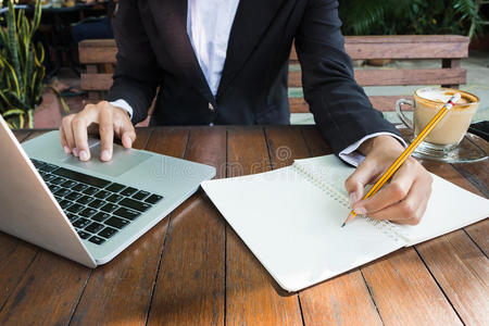 商务女性写在笔记本上，用笔记本电脑在咖啡店的户外工作，复古色调。