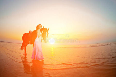 日落时在海滩上骑马的美女。在海边阳光下牵着一匹马的小女孩。