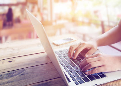 漂亮的年轻时髦女人`手忙着拿笔记本电脑,坐在咖啡店的木桌上照片