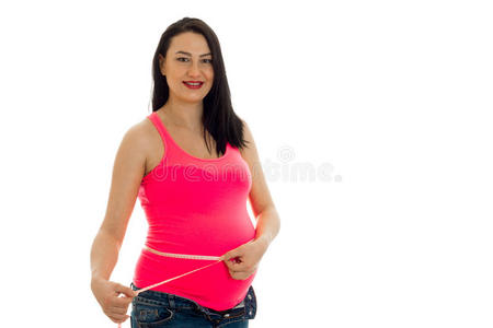 有吸引力的怀孕黑发女人，大腹便便，在白色背景上隔离的粉红色衬衫上的测量磁带