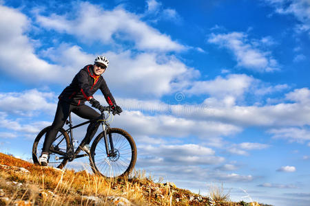 骑自行车的人骑自行车下山。 背景上美丽的天空和云