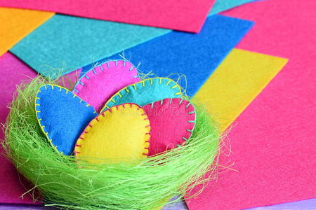 手工剑麻巢与毛毡复活节彩蛋在彩色毡板。 复活节DIY装饰的想法。 有趣的孩子复活节背景