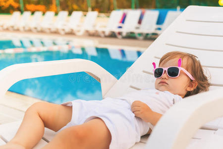 无尽的夏天可爱的婴儿放松在阳光床附近的游泳池，度假村。