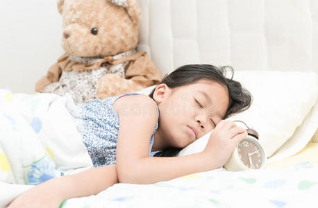 可爱的亚洲小女孩睡在床上触摸闹钟