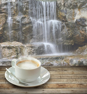 咖啡在白色杯子在木桌上，勺子在瀑布背面