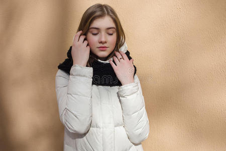 寒冷的季节，年轻美丽的女人闭着眼睛，穿着白色的外套，摆出质感的墙壁，带有光影图案的生活方式自负