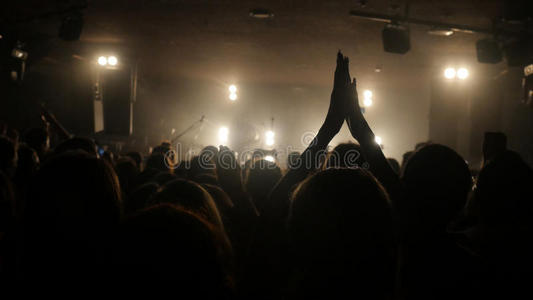 球迷们在夜总会的摇滚音乐会上挥舞着他们的手，在美丽的金色灯光下