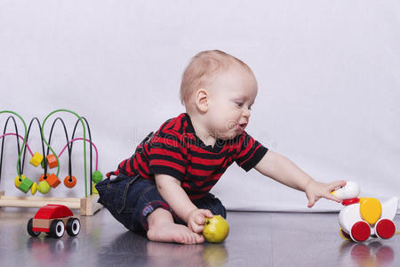 可爱的蹒跚学步的男孩在灰色的地板上玩玩具鸭子