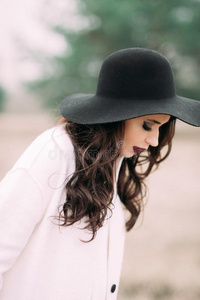 美丽的时尚微笑的女人，戴着黑色的帽子和白色的外套，在大门附近的户外摆姿势