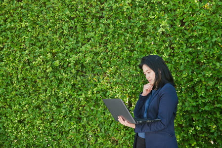 商务女性使用笔记本电脑与绿色树墙背景，伟大的设计或文字，亚洲