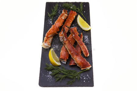 煮熟的蟹腿与柠檬片和在黑色盘子上的白色背景。