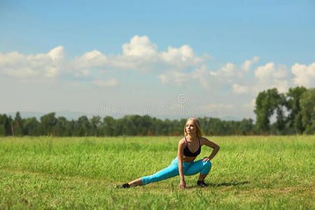 美丽的运动女人在城市公园的绿草中做伸展健身运动。