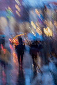 抽象的背景模糊的人在雨伞下，城市街道在雨夜。 有意的运动模糊