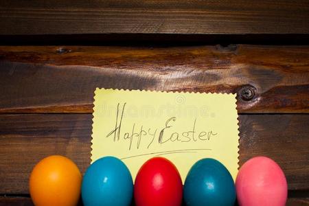 封闭的，用不同明亮的颜色画在自然木制背景上的节日复活节的鸡蛋，上面有一张纸