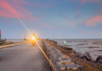 一名男子骑摩托车，头灯开着，在码头