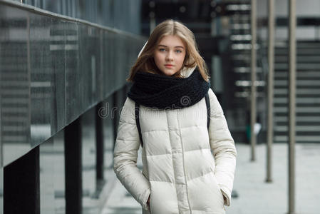 城市肖像年轻美丽的金发时尚女孩在春季秋季户外摆姿势，白色外套，黑色针织围巾。 古董鱼