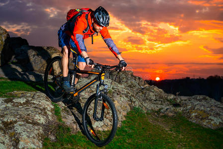 骑山地自行车的人在美丽的日落下沿着春天的岩石山.