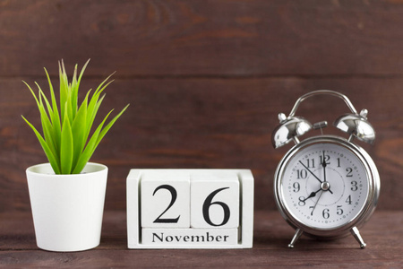 11月26日在木制日历上，木制背景上的闹钟旁边，是上一个秋天的日历日期