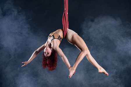 女性运动，性感和灵活的空中马戏团艺术家与红发在空中舞蹈丝绸