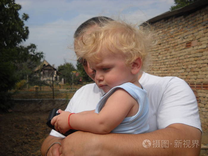 父亲抱着一个金发碧眼的小男孩孩子低头沉思皱着眉头夏天在村里