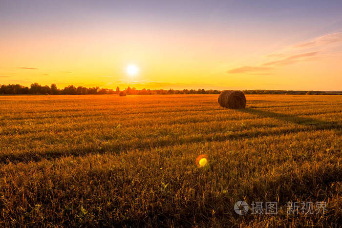 秋天阳光明媚的傍晚田野上的落日和干草堆