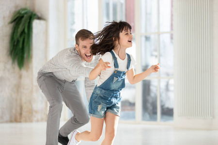 小孩追喜出望外的千禧一代男人追着笑着跑来跑去的小女儿.照片