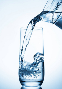 飞溅火星pouring water from glass pitcher on blue background 照片