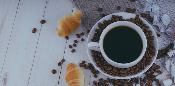 A steaming cup of coffee with coffee beans and a croissant on vi