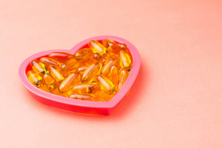 Fishoil capsules in the heart shape frame on pink background 