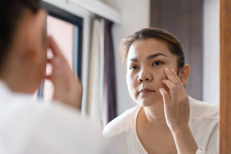 Middle aged asian woman looking at wrinkles in mirror 