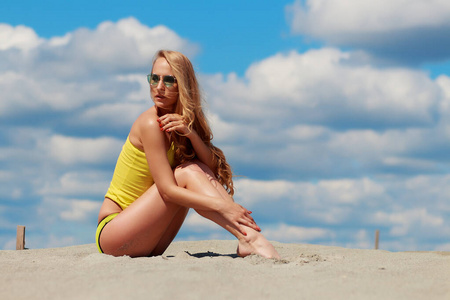 穿着时髦泳装的迷人女人跪在沙滩上