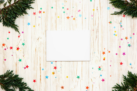 在白色木质背景上，用空白纸圣诞树枝和小彩星组成圣诞构图。平躺。俯视图。