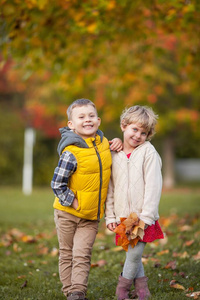 小男孩拥抱一个女孩。快乐的孩子们穿着鲜艳的秋装。秋高气爽。