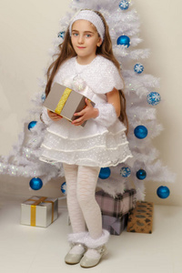 在圣诞树旁拿着礼物的小女孩。
