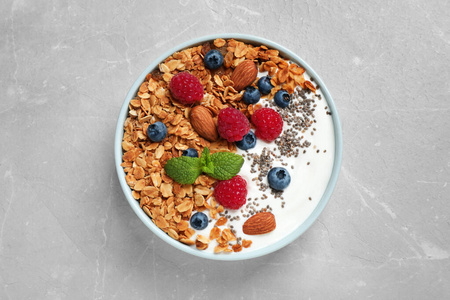 美味的自制格兰诺拉麦片配酸奶和浆果放在浅灰色的桌子上，俯视。健康早餐