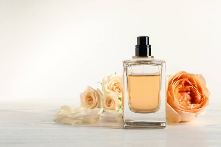 Elegant bottle of perfume and flowers on light background, space