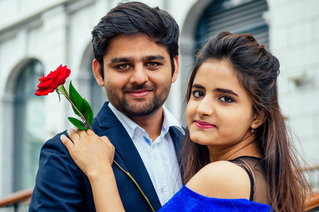 一位身穿蓝色长毛深色连衣裙的印度妇女和她英俊的男朋友在约会。男人在夏天的市中心大街上给他的女朋友送玫瑰