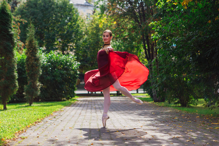 一位穿着红色芭蕾舞裙的女芭蕾舞演员穿着尖头鞋在秋天公园里跳舞。