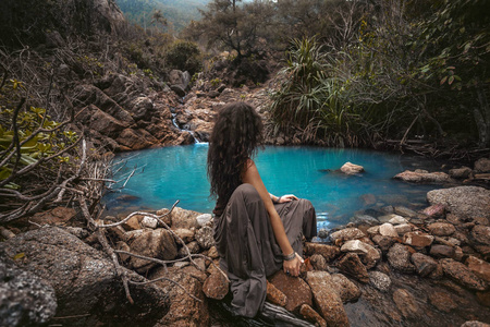 Beautiful young woman sitting at small mountain lake 