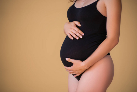 怀孕了闭嘴。怀孕的女孩穿着优雅的黑色连体衣。美丽健康的怀孕。极简主义