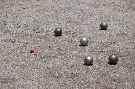 Metallic petanque five balls and a small red wood jack on the gr