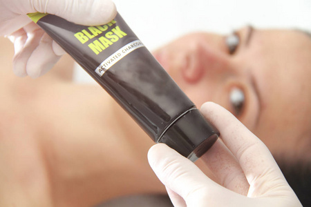 Young beautiful woman applying black charcoal facial mask. Skin 